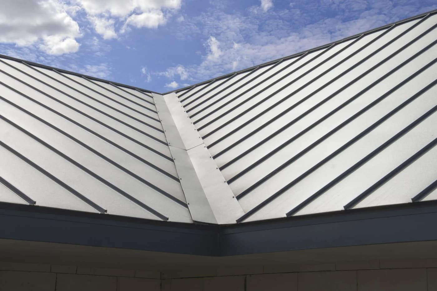 Silver standing-seam metal roof panels meeting at a valley, seen from below