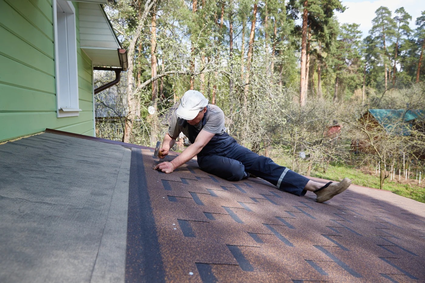 A Man Repairs A Roof Made Of Flexible Tiles On A Sunny Summer Day In A Pine Forest.