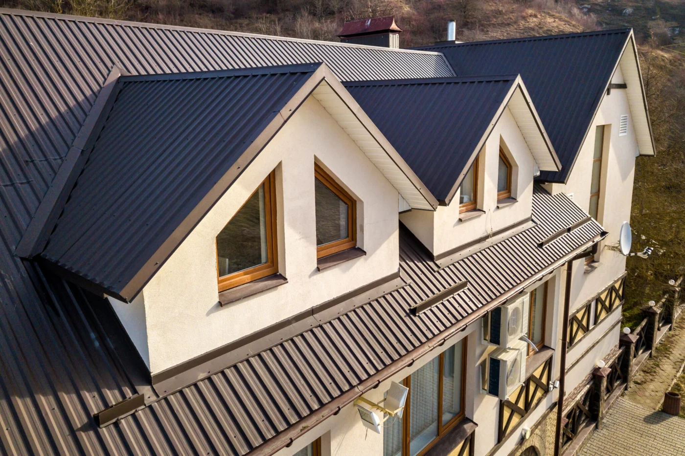 Close Up Aerial View Of Building Attic Rooms Exterior On Metal Shingle Roof, Stucco Walls And Plastic Windows. Close Up Aerial View Of Building Attic Rooms Exterior On Metal Shingle Roof, Stucco Walls And Plastic Windows.