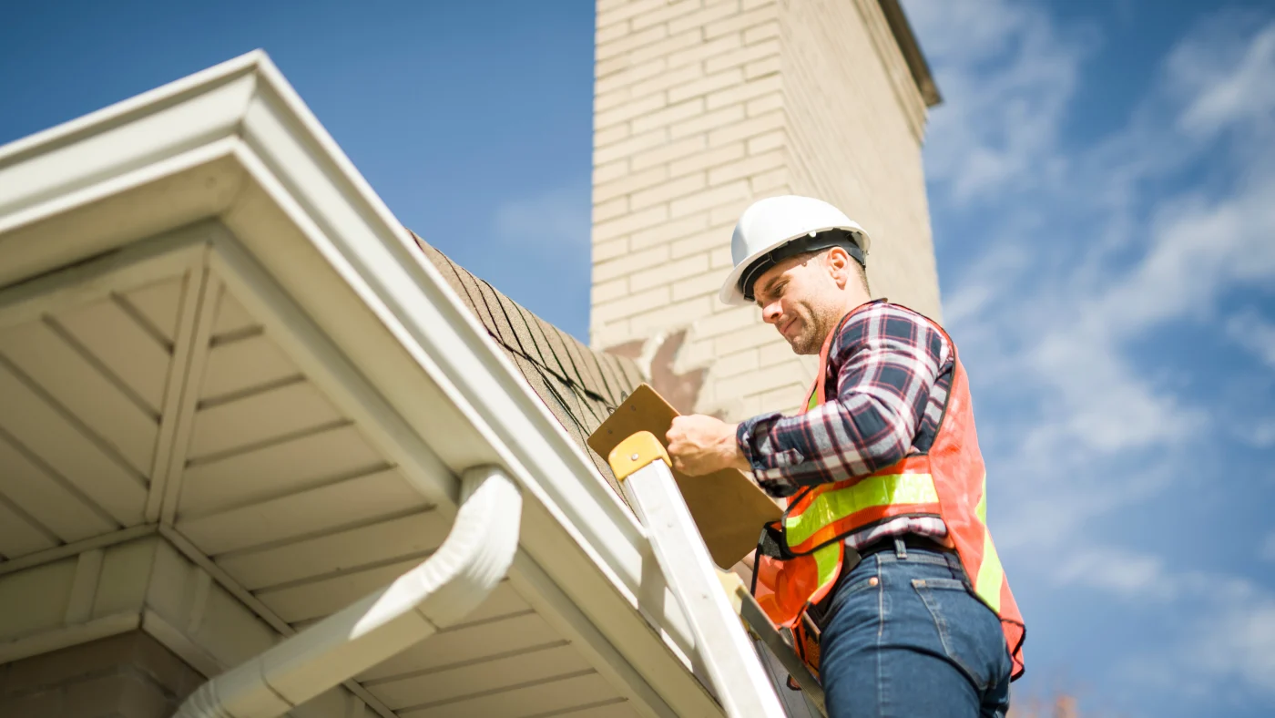 A roofer completing a roof inspection on a ladder with a clipboard