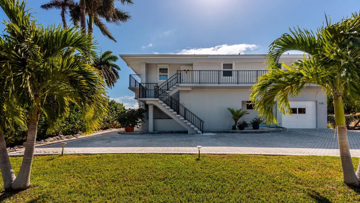 Florida home with grey cement exterior with black stone-coated roof, black and grey tile driveway, and garage