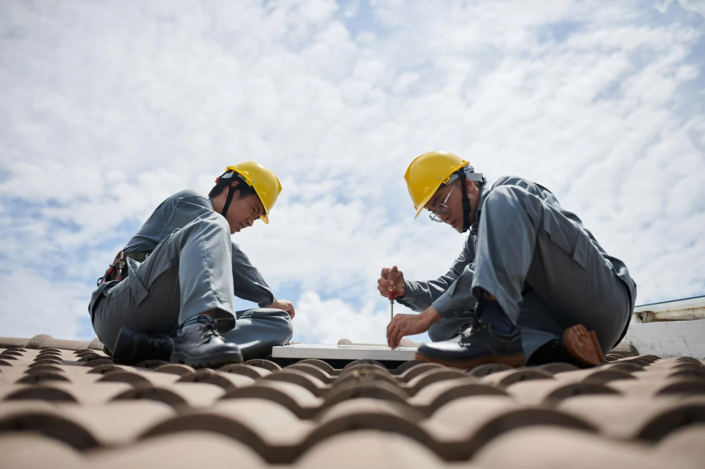 A pair of roofers carefully work on a Spanish tile roof.