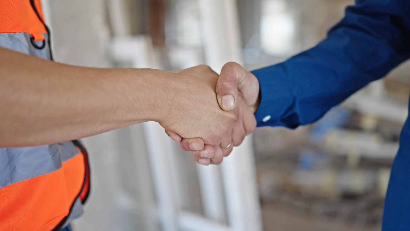 A man in a blue shirt is shaking hands with a construction worker