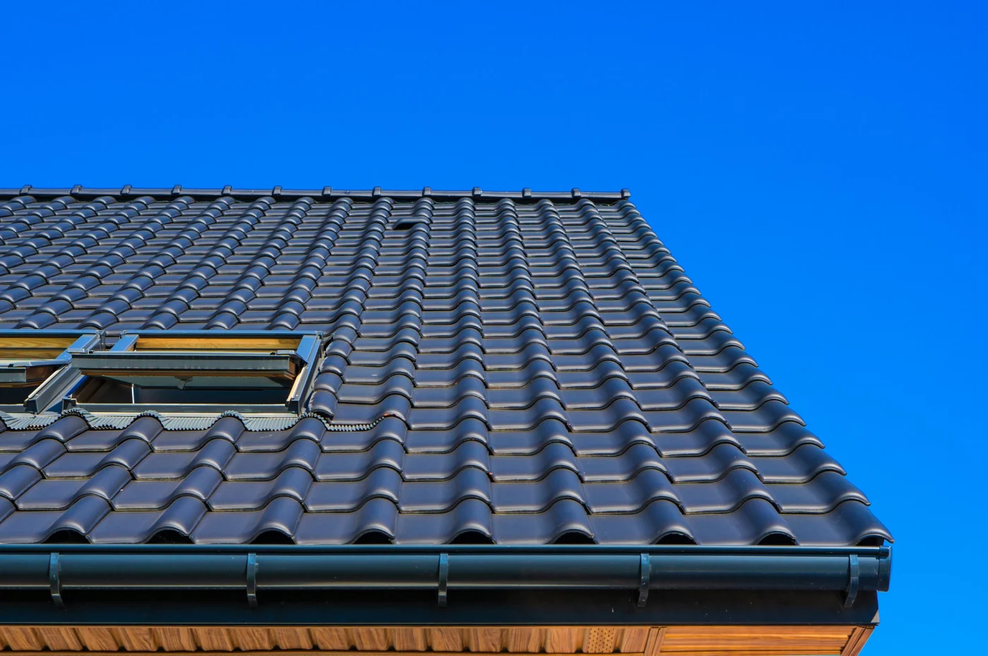 With a dark blue, clear sky, you will see a black, Spanish tile roof. Under the roof, you can see a little peak of the beautiful, wooden siding.