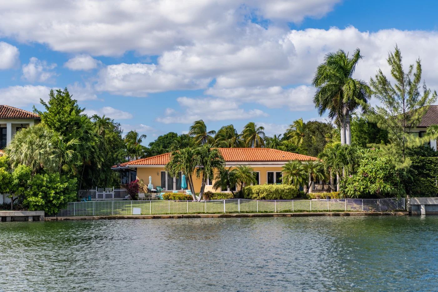 Gorgeous Tile Roofs In Riverview, FL | Universal Roof & Contracting A yellow house with a red Spanish tile roof surrounded by palm trees on the waterfront.
