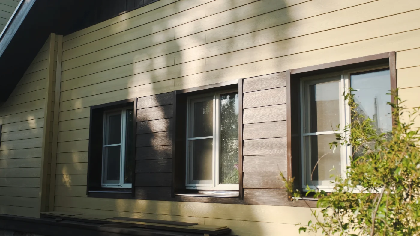 Close-up of a home with yellow and brown siding wrapped around three windows.