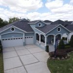 A photo of a home exterior with a dark asphalt shingle roof, gray-blue vinyl siding, and white soffit, fascia, and gutters.