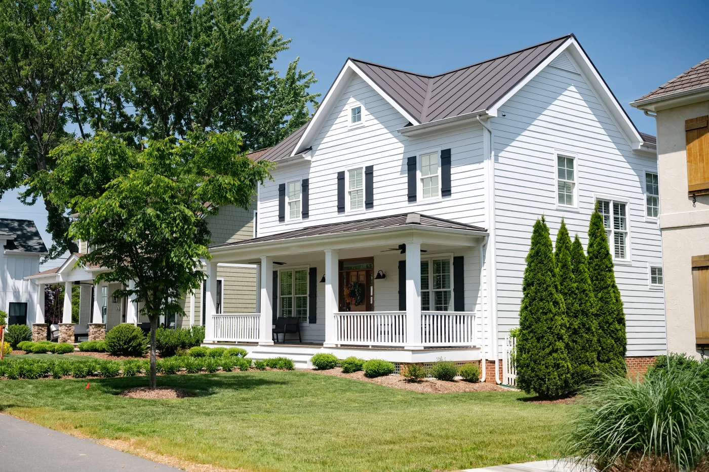 A charming suburban home with a front porch, metal roofing, and white vinyl siding.
