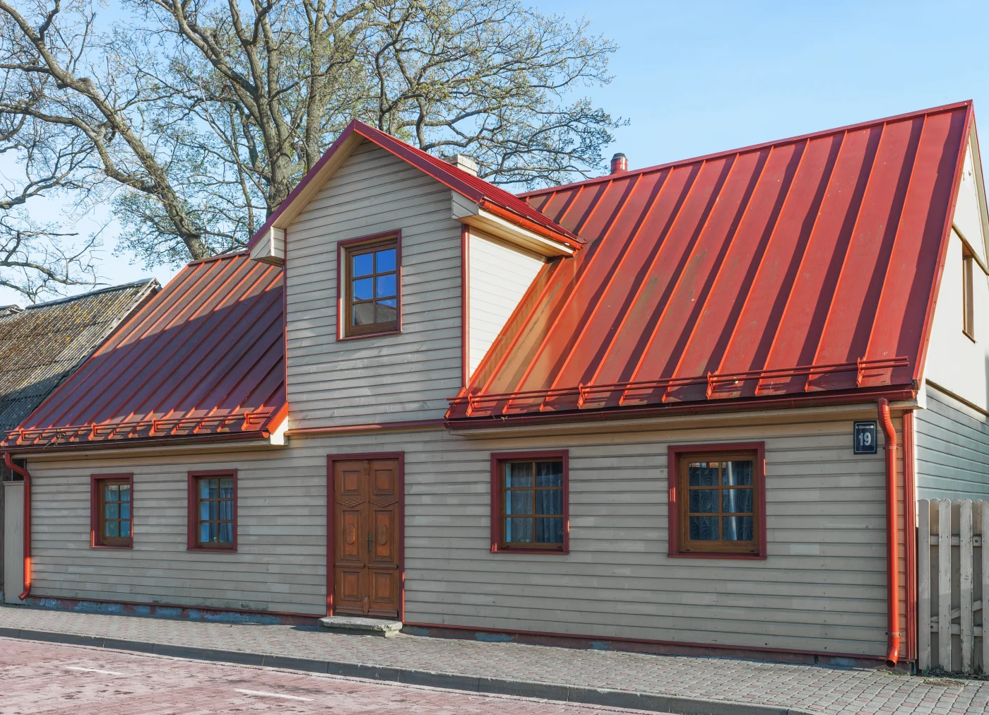 An older, light-tan single-story home with a new, rusty-red-colored metal roof