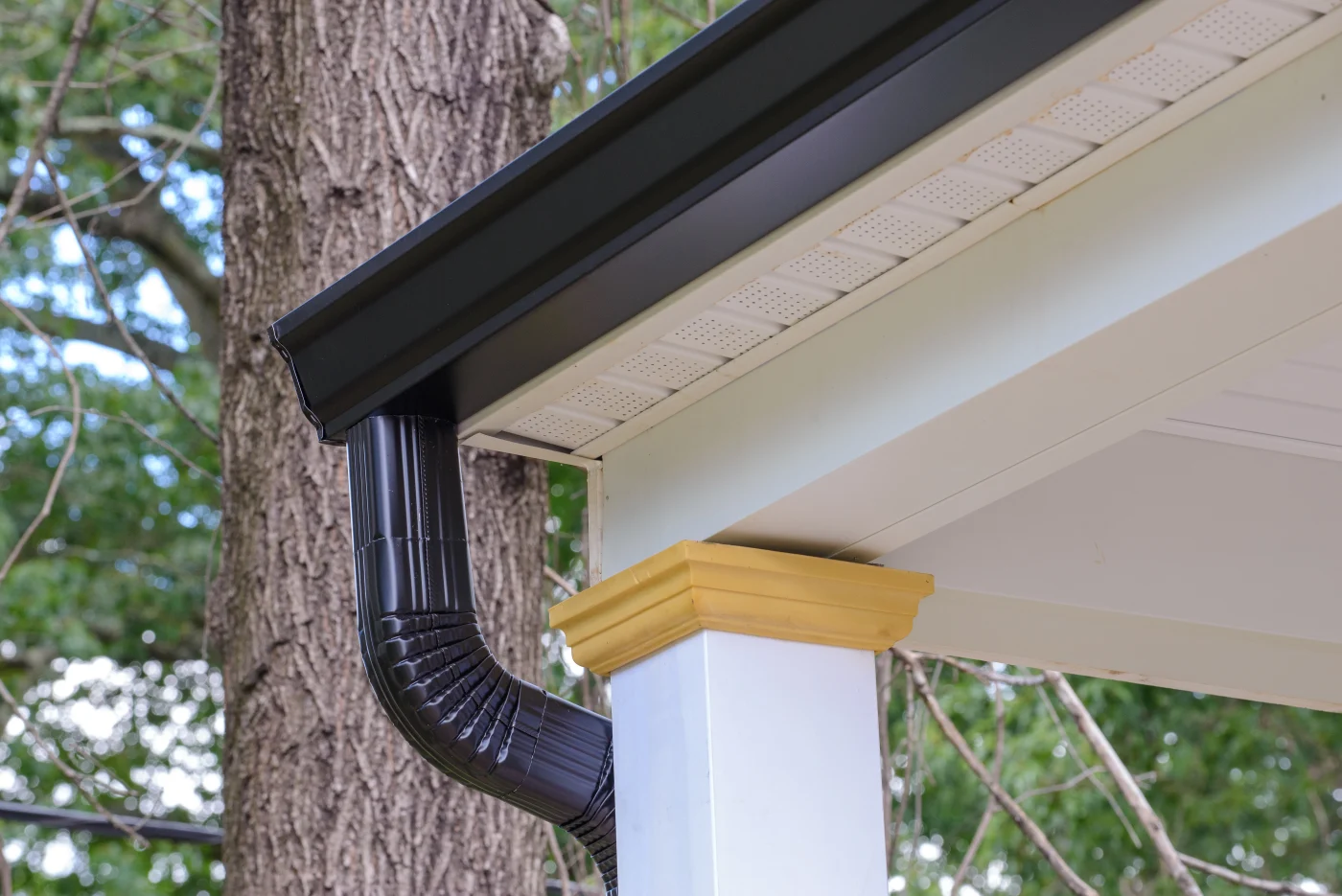 A black rain gutter and downspout attached to a white house with a column.