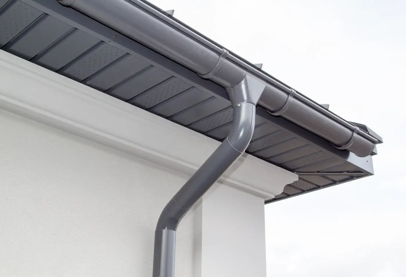 Close-up of white seamless gutters on a building with white horizontal lap siding.