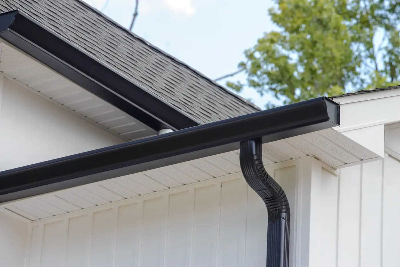 The underside of a residential roof, revealing white board-and-batten siding, soffits, and gray gutters.