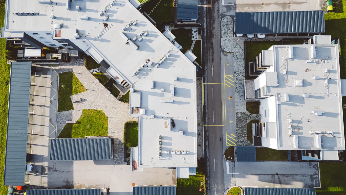 Amazing Commercial Roofing | St. Augustine, FL Aerial view of multiple commercial buildings with bright white flat roofing, surrounding green spaces, parking areas, and walkways.