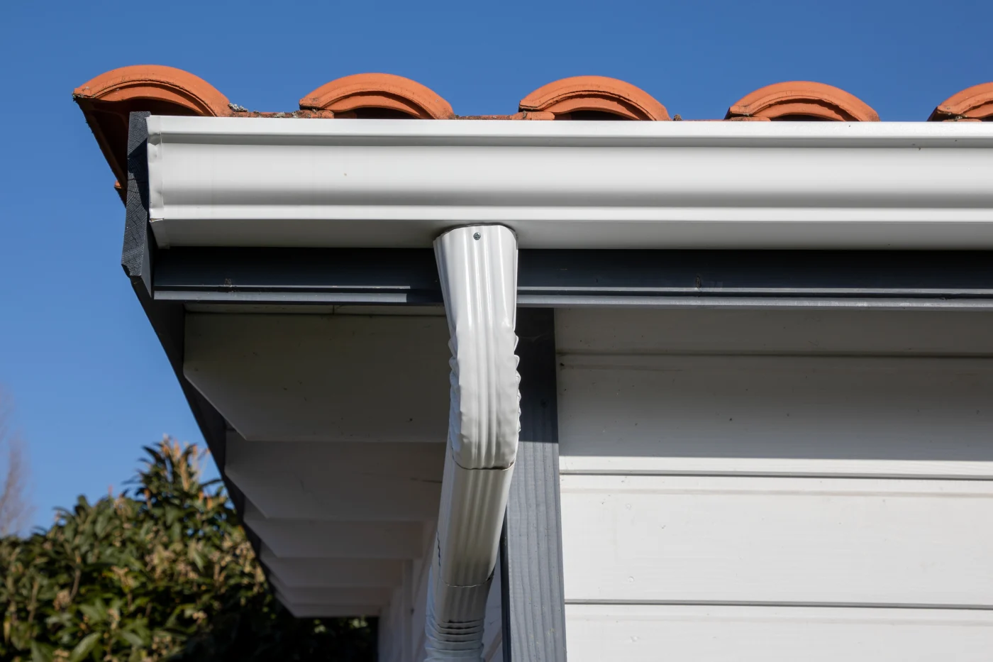 Amazing Siding, Soffit, Fascia, and Gutters | Riverview, FL | Universal Roof and Contracting Close-up view of a home’s white gutter system attached beneath a light soffit, featuring terracotta roof tiles above and a clear blue sky in the background.