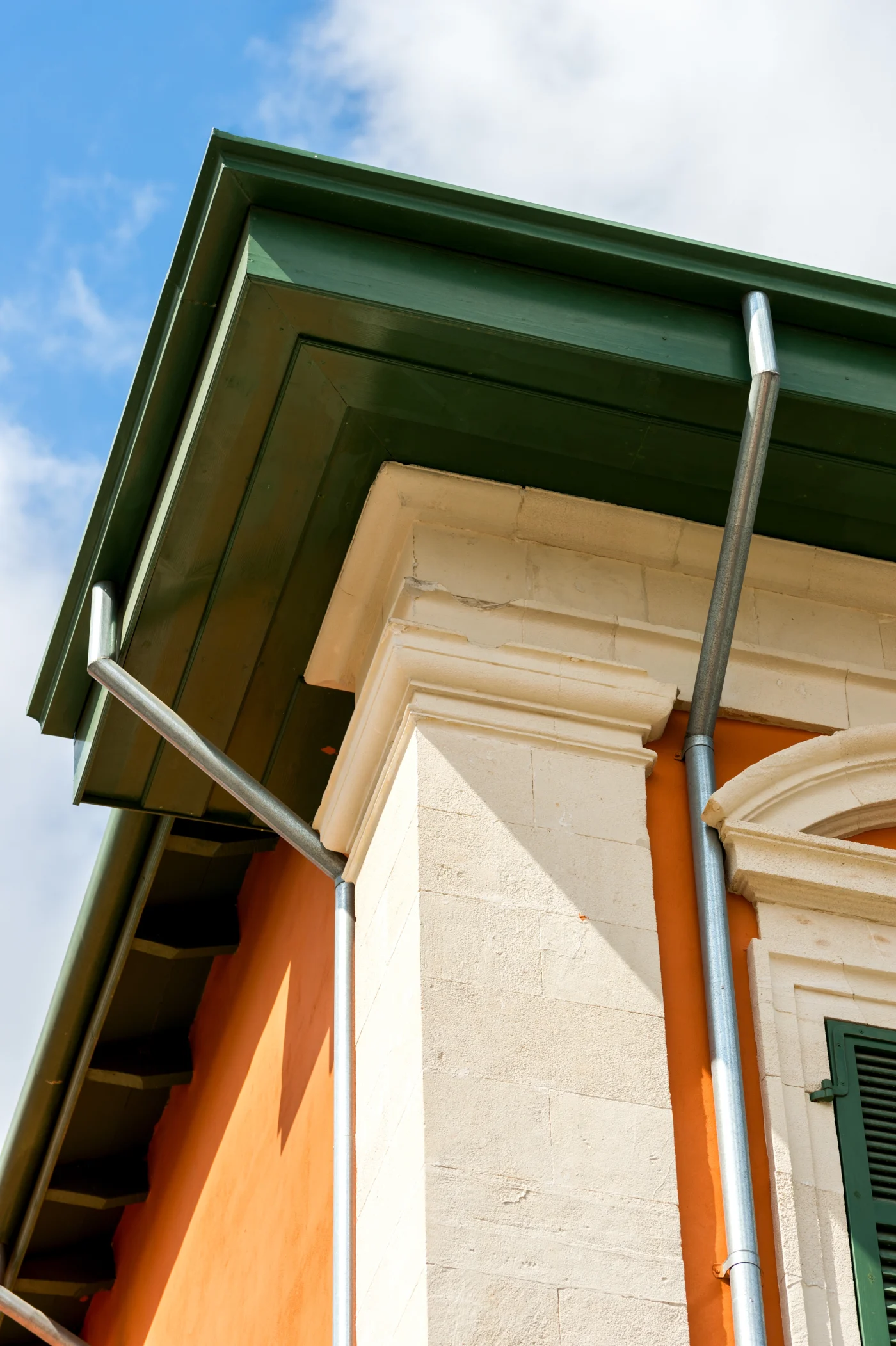 Astounding Siding, Soffit, Fascia, and Gutters | Riverview, FL | Universal Roof and Contracting Close-up view of a home's exterior corner featuring green fascia boards, exposed soffit, and silver downspouts.
