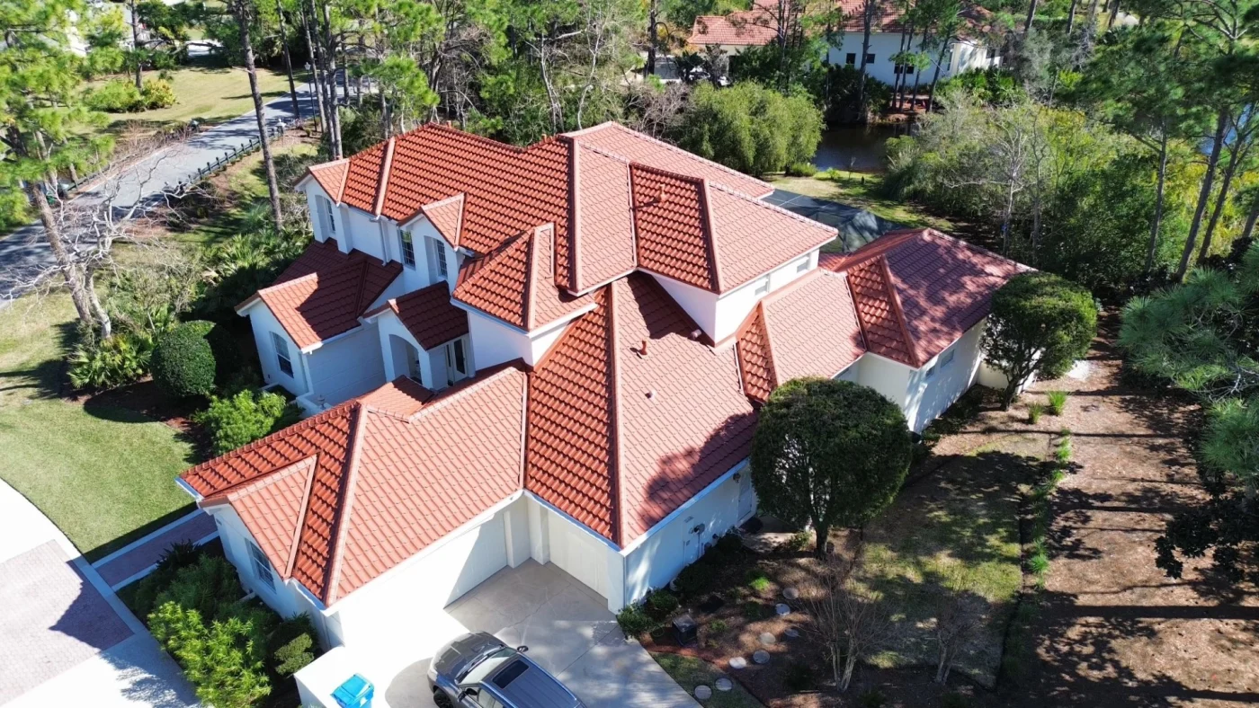 Beautiful Tile Roofing | Macclenny, FL | Universal Roof and Contracting Mediterranean-style home with terracotta tile roof and white stucco exterior, surrounded by tall pine trees and landscaped grounds, aerial view.