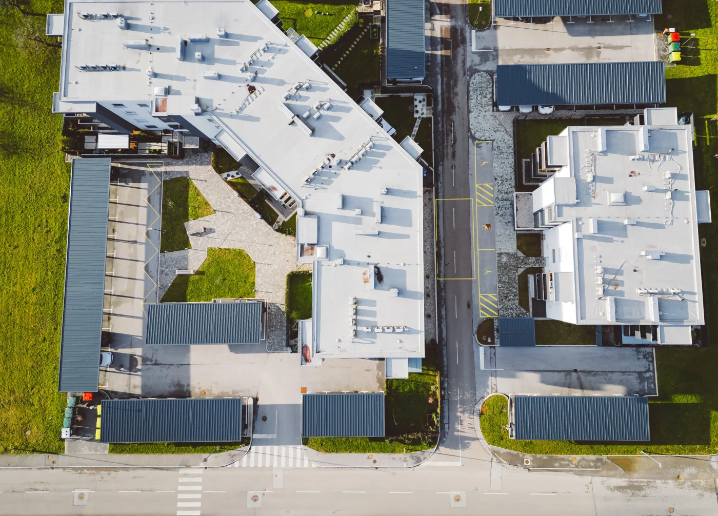 Dependable Commercial Roofing | Fernandina Beach, FL | Universal Roof and Contracting Overhead view of commercial buildings with white flat roofs, surrounding green spaces, paved walkways and parking areas with covered structures.