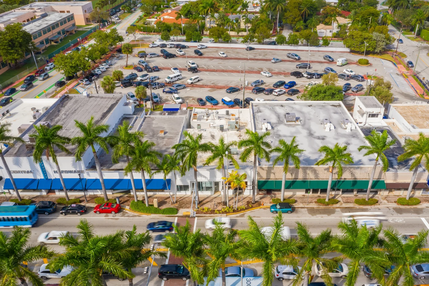 Perfect Commercial Roofing | Bradenton, FL | Universal Roof and Contracting Aerial view of commercial buildings with flat roofs lined by tall palm trees, with busy traffic and a large parking lot in the background.