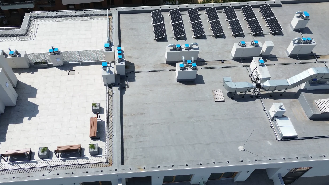Regal Commercial Roofing | Fernandina Beach, FL Aerial view of a commercial building’s flat roof featuring solar panels, HVAC units, ventilation systems, and a fenced rooftop patio area with benches and planters.