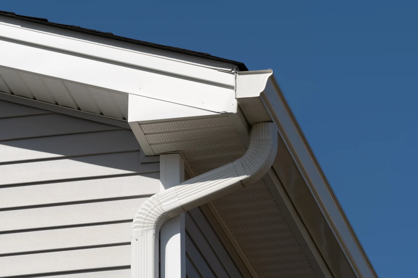Spectacular Siding, Soffit, Fascia, and Gutters | Bradenton, FL | Universal Roof and Contracting Close-up view of a home's exterior showing white vinyl siding, soffit, fascia, and an attached downspout