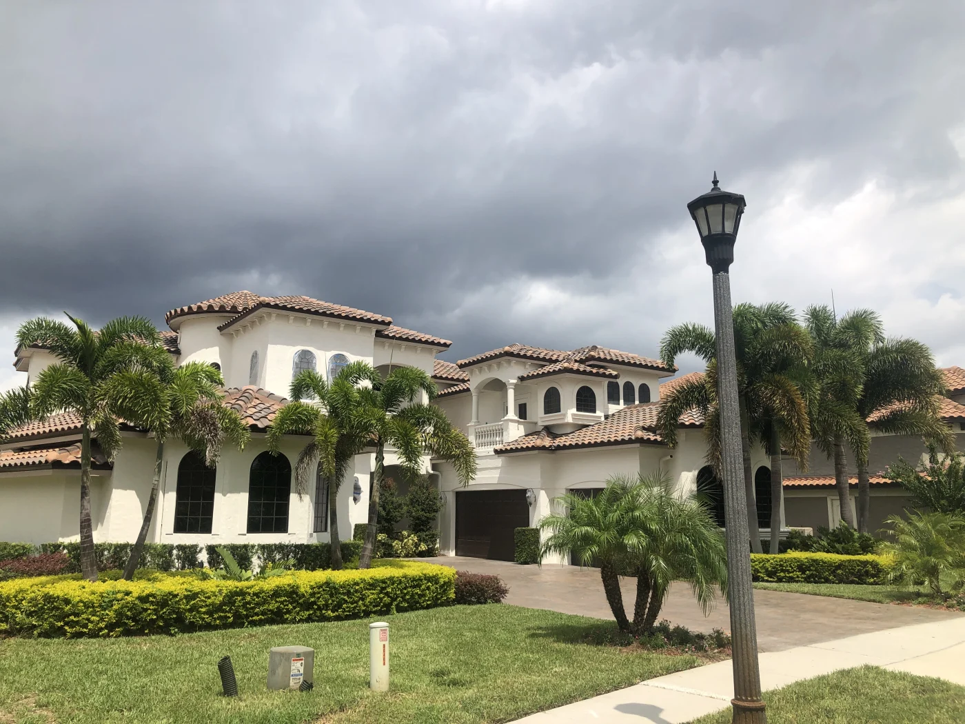 Elegant Tile Roofs | Apopka, FL | Universal Roof A luxurious white Mediterranean-style home with multiple tan clay tile roof sections, surrounded by palm trees and manicured landscaping.