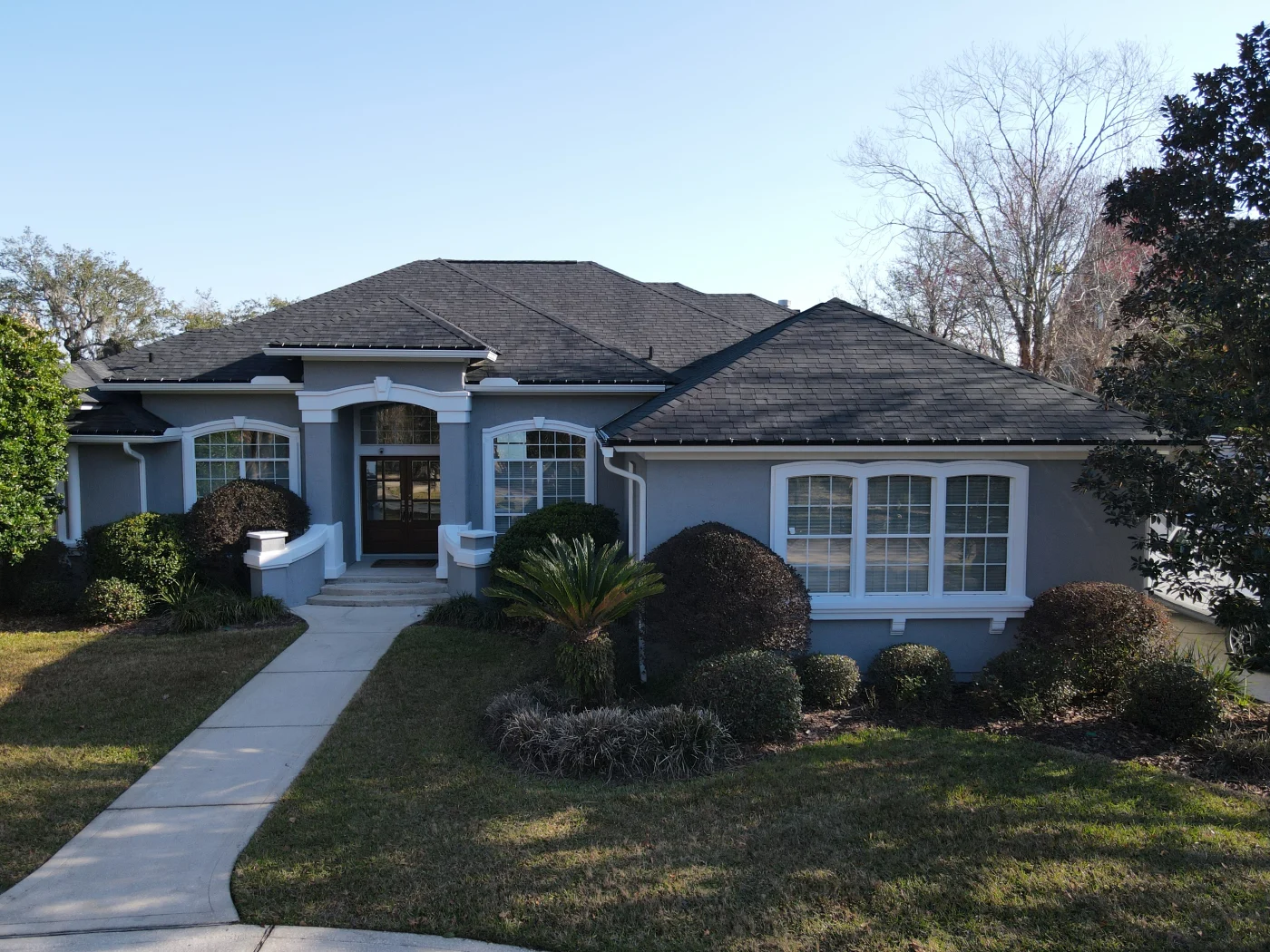 Gorgeous Asphalt Shingles |Winter Park, FL | Universal Roof & Contracting Front view of a gray stucco home with a dark asphalt shingle roof, white trim, large front windows, manicured shrubs, and a curved walkway.