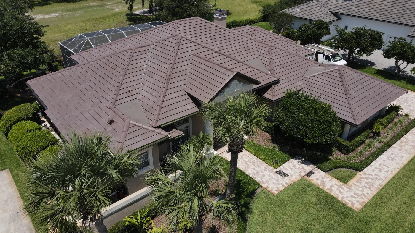 Default A high-angle aerial view of a home with a brown tile roof featuring multiple ridges and valleys, surrounded by palm trees.