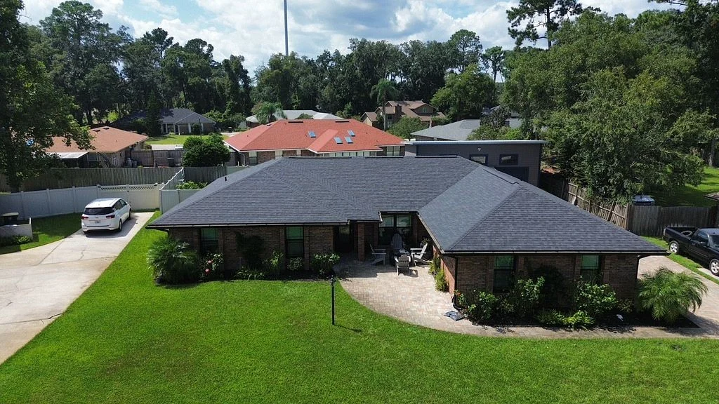 An aerial view of a completed roof replacement on a single-story brick home in Florida. The sleek black asphalt shingles contrast with the bright green lawn and surrounding neighborhood, showcasing both durability and curb appeal delivered by Universal Roof & Contracting.