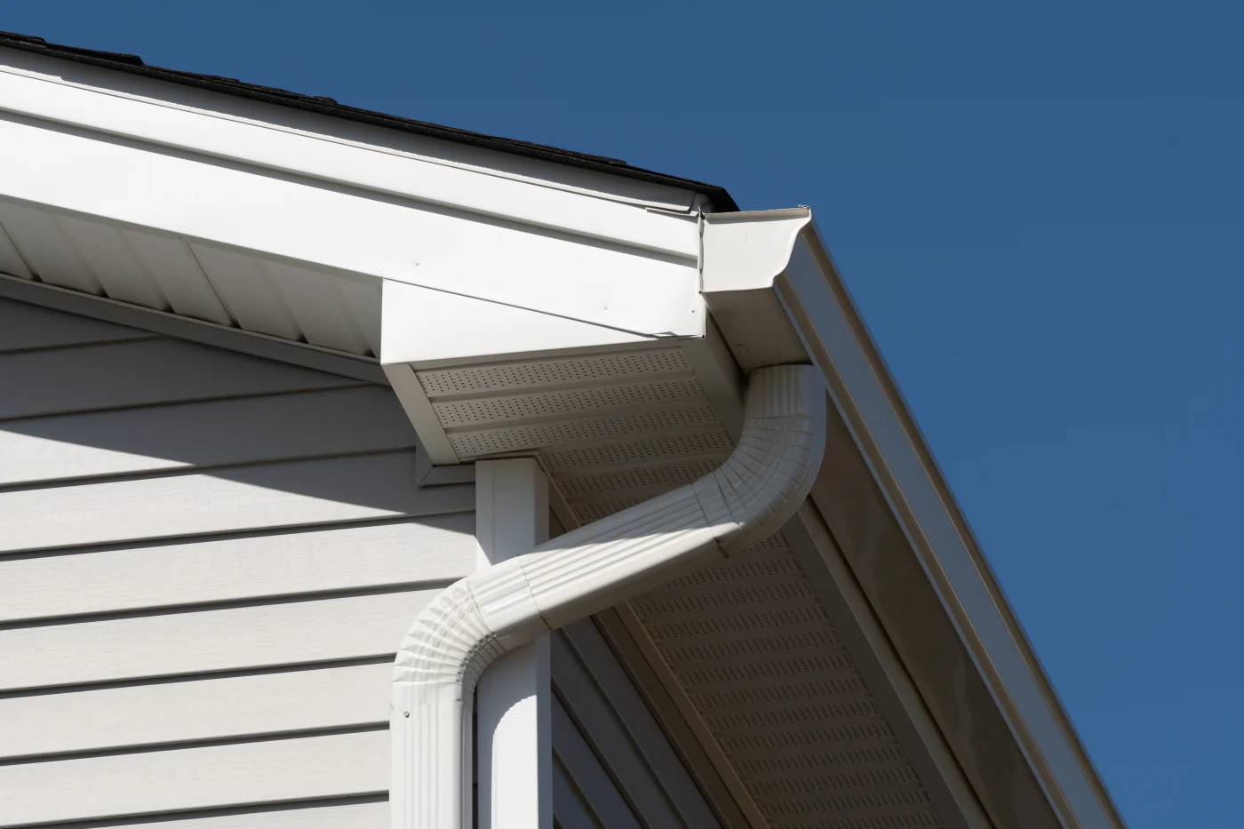 Spectacular Siding Soffit Fascia and Gutters | Cocoa Beach, FL Close-up view of a home’s exterior in Cocoa Beach, FL, showing white siding, soffit, fascia, and a connected downspout against a clear blue sky.
