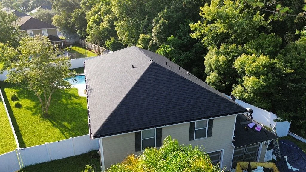 Stupendous Asphalt Shibgles | Cocoa Beach, FL Aerial view of a two-story Cocoa Beach, FL home with a newly installed asphalt shingle roof, surrounded by trees, a fenced yard, and a neighboring backyard pool.