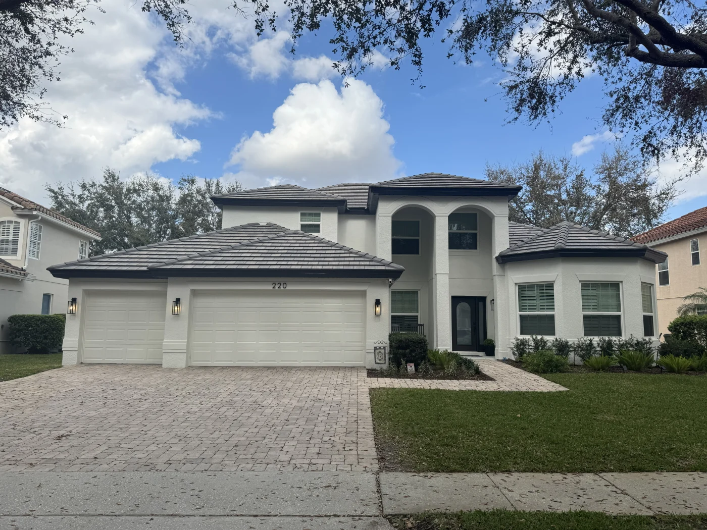 Amazing Residential Roofing Company | Westchase, FL | Universal Roof and Contracting Front view of a large white two-story stucco home with a dark tile roof, three-car garage, paver driveway, and neatly maintained front lawn.