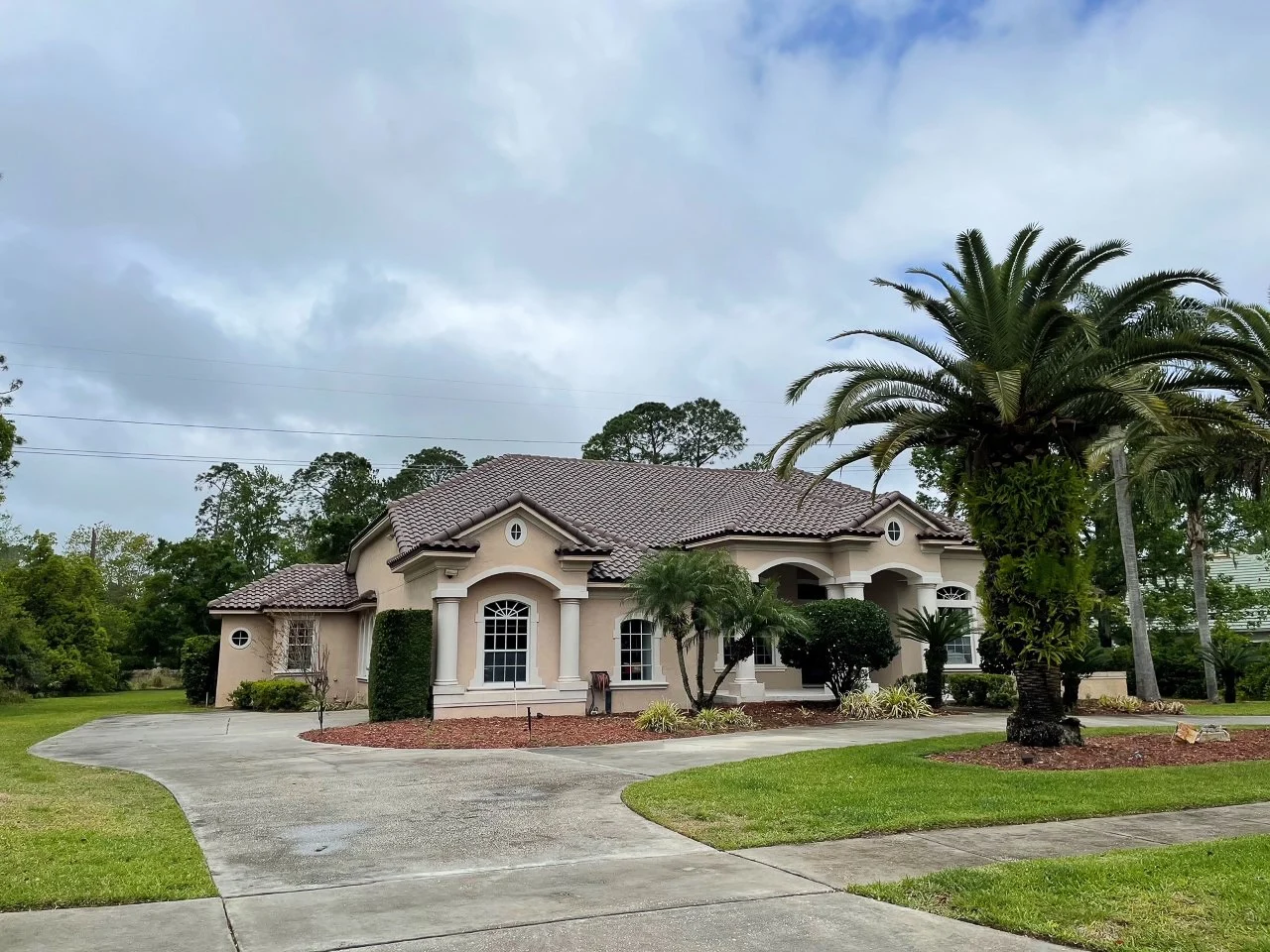 Spectacular Residential Roofing Services | Ponte Vedra Beach, FL | Universal Roof and Contracting Mediterranean-style stucco home in Ponte Vedra Beach, FL, with a brown tile roof, arched windows and entryway, and a wide curved concrete driveway.